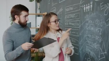 Tebeşir tahtasında yazan kız ve erkek modern ofiste konuşan bilgiyi analiz ediyorlar.