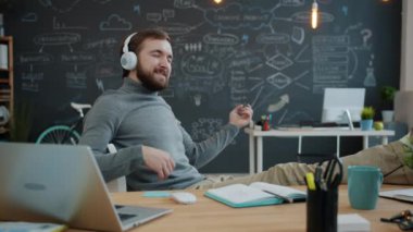 Yaratıcı ofiste gitar çalıyormuş gibi yapıp kulaklıkla müzik dinleyen oyuncu.