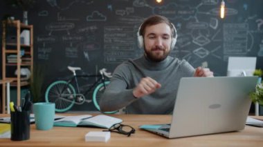 Ofis çalışanı çekici adam kulaklıkla müzik dinliyor iş yerinde dans ediyor.