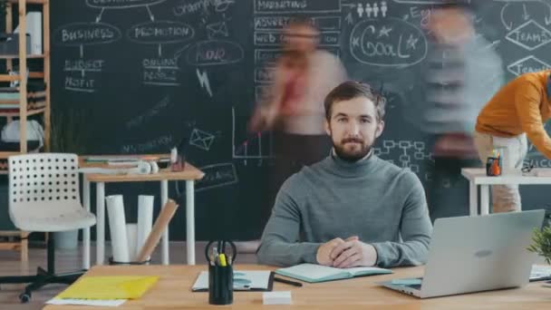 Retrato de lapso de tempo de homem ambicioso na mesa em escritório de espaço aberto com pessoas trabalhando ao redor — Vídeo de Stock