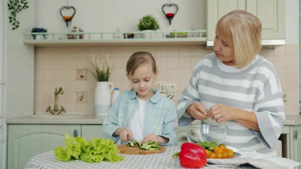 Linda niña y anciana abuela cocina ensalada en la mesa de la cocina juntos — Vídeos de Stock