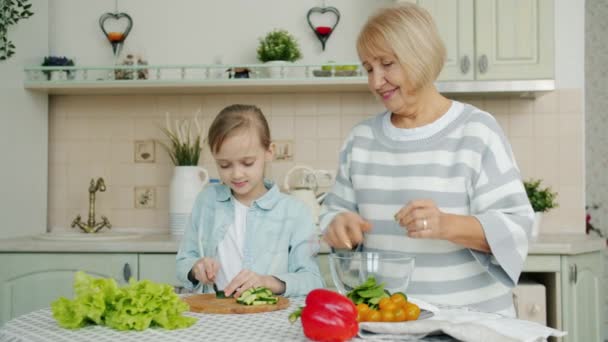 Nieta y abuela haciendo ensalada juntos y hablando en la cocina en casa — Vídeos de Stock