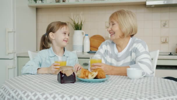 Enfant et grand-mère cliquetis verres avec du jus et rire à la table de cuisine — Video