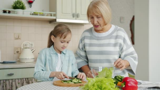 Granny and kid preparing salad cutting vegetables and chatting bonding at home — Stock Video