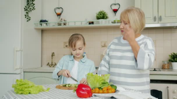 Cámara lenta de niña cortando verduras y alimentando a la abuela con pepino — Vídeos de Stock