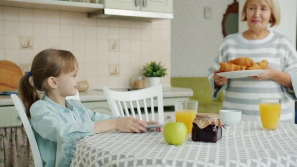 Grand-mère attentionnée apportant assiette avec croissants frais nourrir petite-fille à la maison dans la cuisine — Video