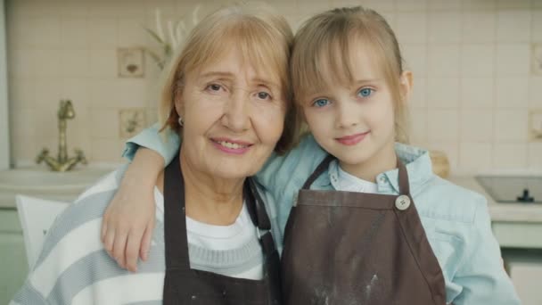 Portrait de grand-mère et petite-fille dans des tabliers souriant regardant la caméra dans la cuisine — Video