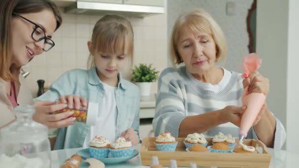 Cámara lenta de la mujer mayor, la joven y el niño decorando cupcakes en casa — Vídeos de Stock