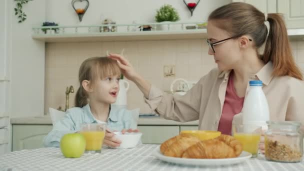 Liten flicka som äter frukost och pratar med mamma sitter vid bordet i köket i lägenhet — Stockvideo