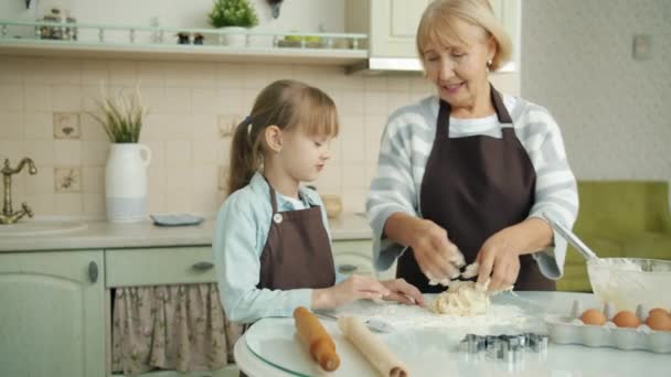 Old woman in apron mixing dough and talking to little granddaughter at home in kitchen — Stock Video