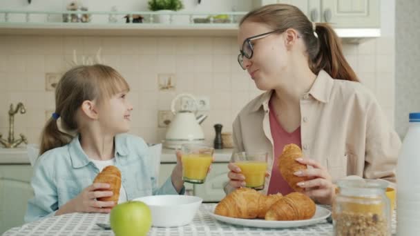 Moeder en dochter ontbijten croissants en drinken sapglazen thuis — Stockvideo