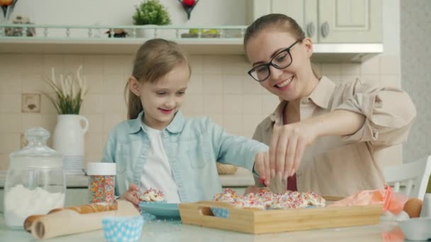Мать и дочь украшают кексы на кухне, обсуждая приготовление пищи дома — стоковое видео