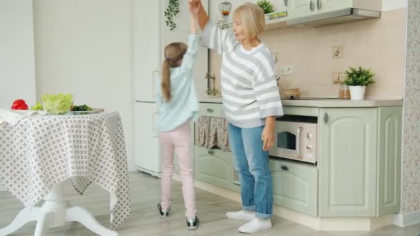 Niña bailando con la abuela en la cocina, anciana mostrando pulgares hacia arriba — Vídeos de Stock