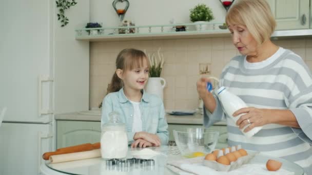 Amar a la abuela enseñando a la nieta cómo hacer pastelería añadiendo ingredientes al tazón — Vídeos de Stock