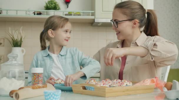 Mujer joven y niña cocinando cupcakes decorando pasteles y charlando en la cocina — Vídeos de Stock