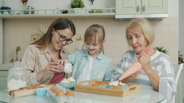 Barn, mor och mormor dekorerar muffins och pratar i köket — Stockvideo