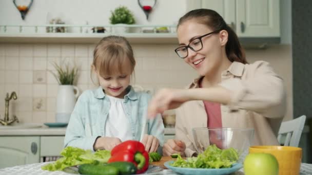 Mor och dotter gör sallad med färska grönsaker och pratar i köket — Stockvideo