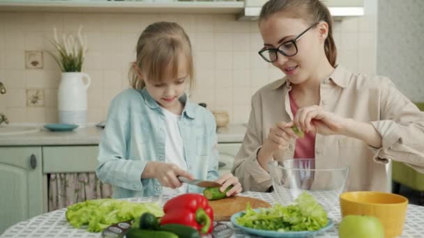 Söt liten flicka hjälpa mamma i köket skära grönsaker för sallad och prata — Stockvideo