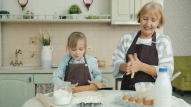 Tatlı çocuk mutfakta kurabiye hazırlıyor büyükanneye yardım ediyor sonra da eğleniyor ve gülüyor.