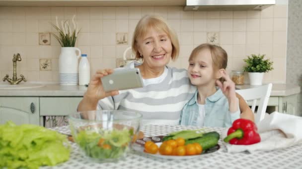 Mormor och barnbarn tar selfie i köket med smartphone kamera — Stockvideo