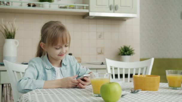 Enfant mignon utilisant un smartphone lorsque la mère apporte une assiette de croissants frais dans la cuisine — Video
