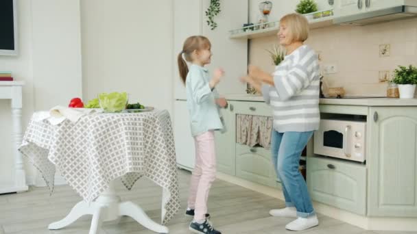 Αργή κίνηση ευτυχισμένης γιαγιάς και εγγονής χορεύουν διασκεδάζοντας στην κουζίνα στο σπίτι — Αρχείο Βίντεο