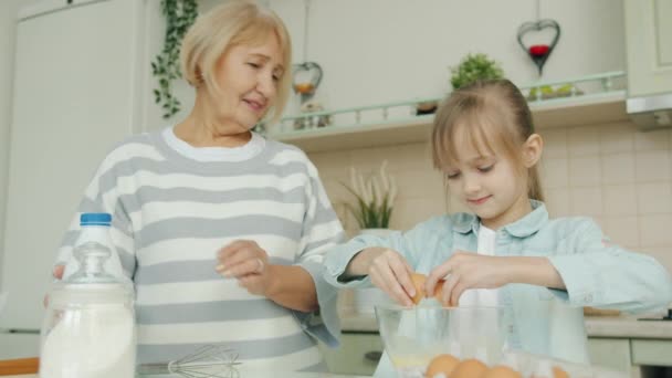 Bedårande flicka och äldre dam matlagning tillsammans i köket gör deg och prata — Stockvideo