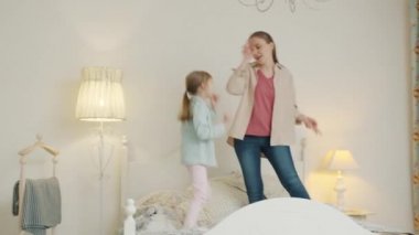 Neşeli bir çocukla yatakta dans eden mutlu genç bir kadın zıplayarak gülerek müzikten zevk alıyor.