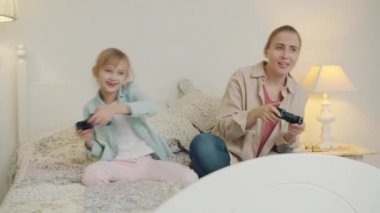 Neşeli kadın ve küçük kız video oyunu oynuyorlar zaferi kutluyorlar yatakta eğleniyorlar