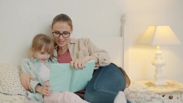 ケア母読書本へ可愛いです女の子座っているベッドルームで一緒に — ストック動画