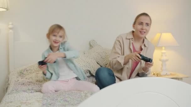 Χαρούμενη γυναίκα και κοριτσάκι παίζουν βιντεοπαιχνίδι γιορτάζοντας τη νίκη διασκεδάζοντας στο κρεβάτι — Αρχείο Βίντεο