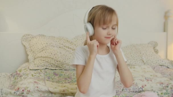 Boldog gyerek élvezi a zenét a fejhallgató mozgó fej pihentető ágyban lakásban — Stock videók