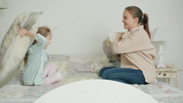 Медленное движение матери и дочери, дерущихся подушек, веселящихся в спальне, наслаждающихся отдыхом — стоковое видео