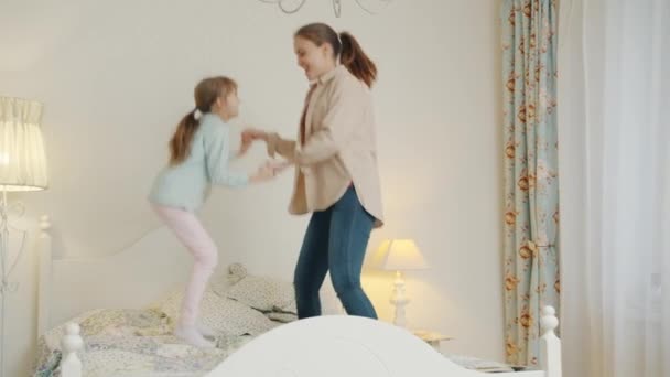 Mãe ativa jovem mulher se divertindo com a filhinha fofa em casa pulando na cama — Vídeo de Stock