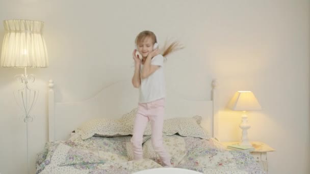 Slow motion van speels kind dansen en springen op bed het dragen van een koptelefoon hebben plezier alleen — Stockvideo