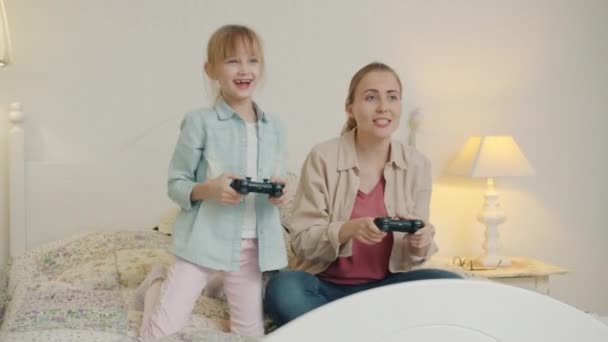 Mamma spelar TV-spel med dotter och sen gör high-five i sängen i sovrummet — Stockvideo