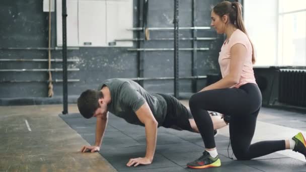 Homme fort faisant push-ups dans la salle de gym Crossfit tandis que l'entraîneur jeune femme parlant étudiant motivant — Video