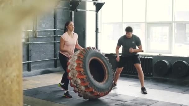 Meisje in sportkleding tillen en flippen zware rubberen band uit te werken met coach in de sportschool — Stockvideo