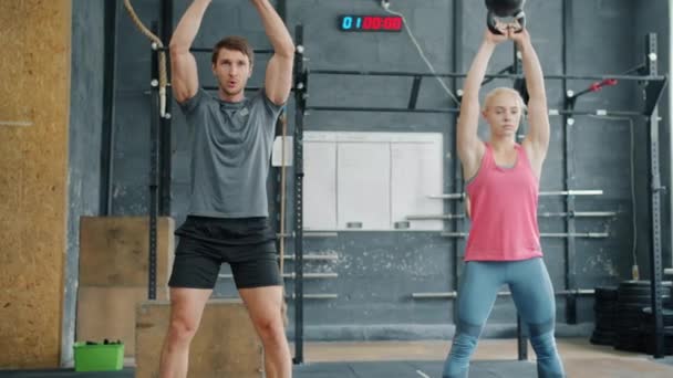 Lány és fiú edzés kettlebells guggoló emelés súly edzés bent együtt — Stock videók