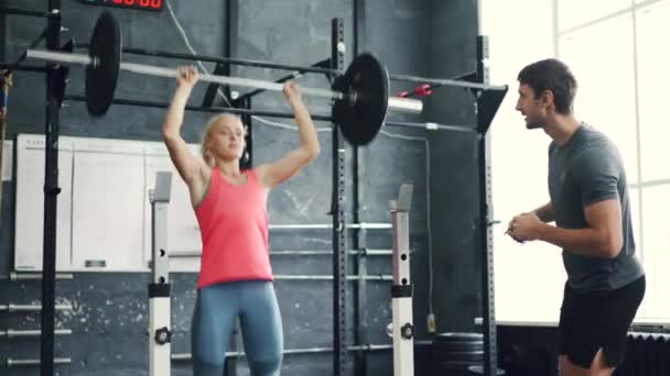 Muscular chica levantamiento pesado barbell bajo entrenador orientación en moderno gimnasio — Vídeos de Stock