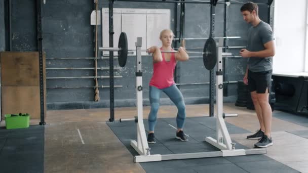 Forte allenamento femminile con bilanciere accovacciato con traversa pesante che si allena in palestra con allenatore — Video Stock