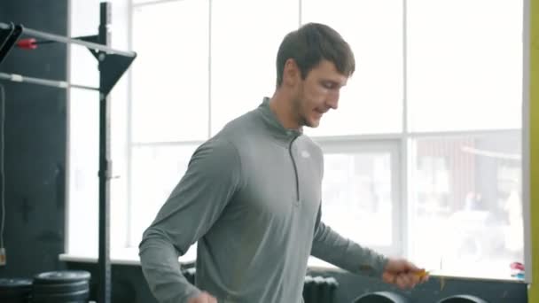 Young guy in sportswear jumping with skipping rope in gym working out alone — Stock Video