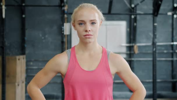 Повільний рух красивої дівчини в спортивному одязі, стоячи в приміщенні в спортзалі і дивлячись на камеру — стокове відео