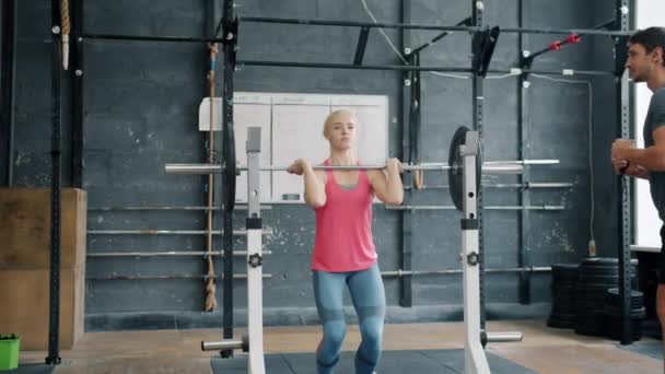 Feminino musculação formação no ginásio com treinador bonito cara levantando barbell — Vídeo de Stock