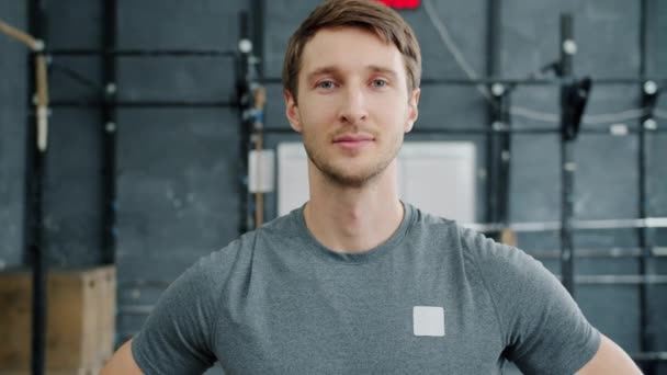 Porträtt av attraktiv ung man idrottsinstruktör bär sportkläder i gymmet tittar på kameran — Stockvideo