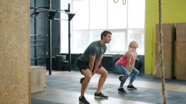 Spor salonunda çömelmiş, kettlebell egzersizleri yapan genç çiftlerin ağır çekimleri.