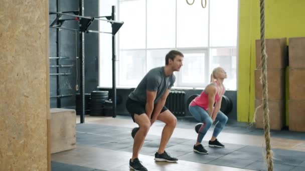 Movimiento lento de pareja joven haciendo ejercicio en el gimnasio en cuclillas con pesas haciendo ejercicio — Vídeo de stock