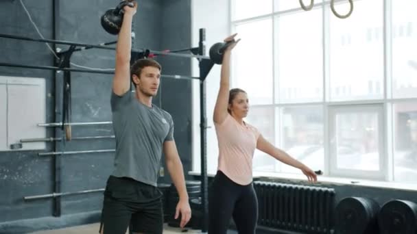 Mladý pár trénink v posilovně vzpírání squatting s kettlebells dohromady — Stock video