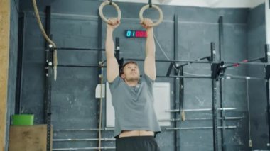 Çapraz antrenman sırasında spor salonunda halkalar üzerinde alıştırma yapan genç bir adam.