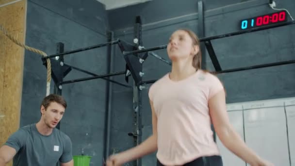 Cámara lenta de la señora bonita haciendo deportes en el gimnasio saltando con saltar la cuerda de entrenamiento con entrenador masculino — Vídeos de Stock